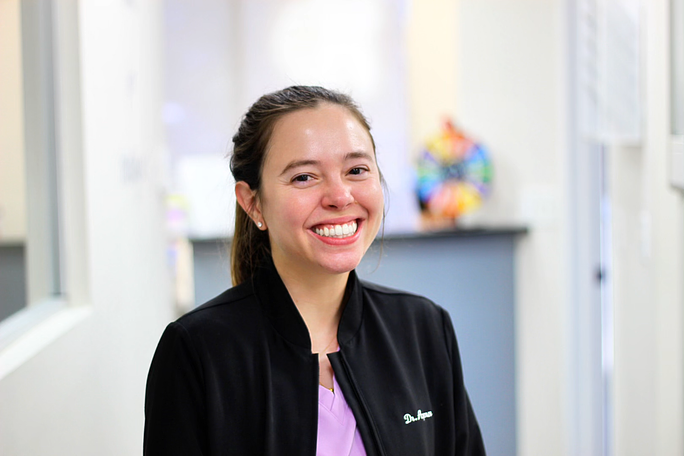 Smiling person in a black jacket standing in a bright hallway