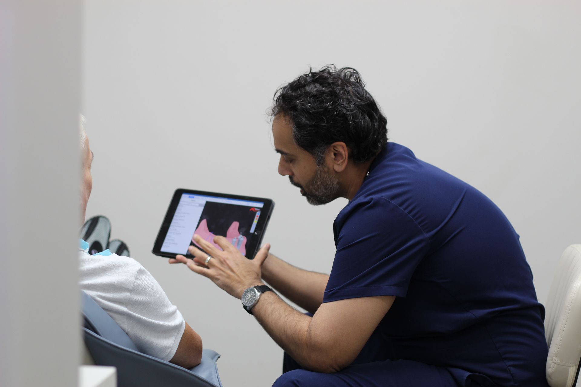 Person showing something on a tablet to another seated person in a clinical setting