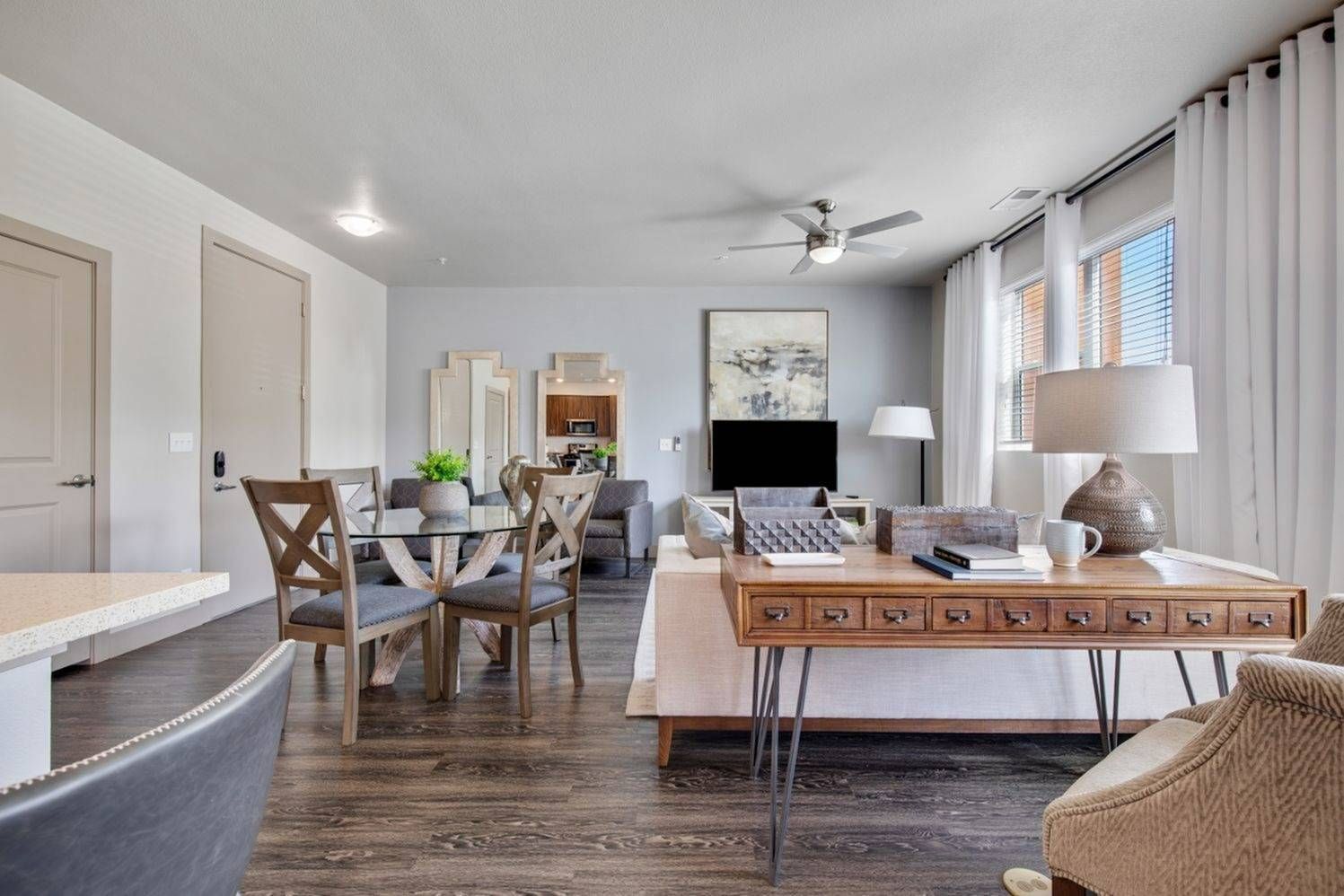 Modern apartment with wood cabinets, stainless steel appliances, and island, opening to a living area with fan and artwork.