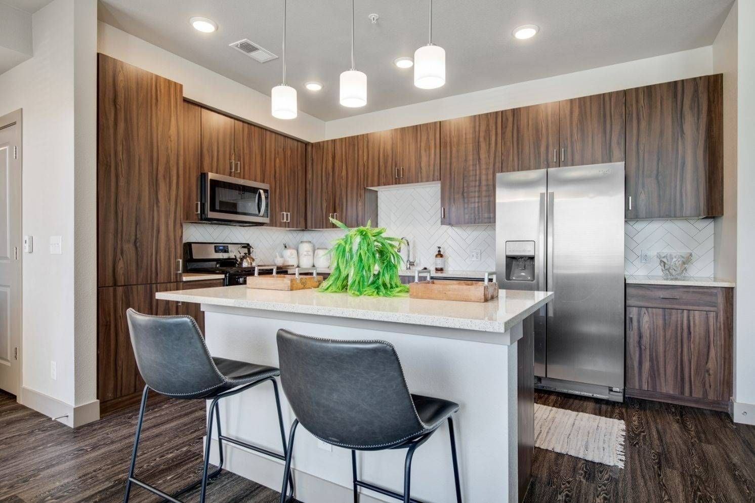 Modern kitchen with wood-grain cabinets, stainless steel appliances, island bar, and pendant lighting.