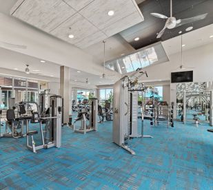 A large gym with a lot of exercise equipment and a ceiling fan.