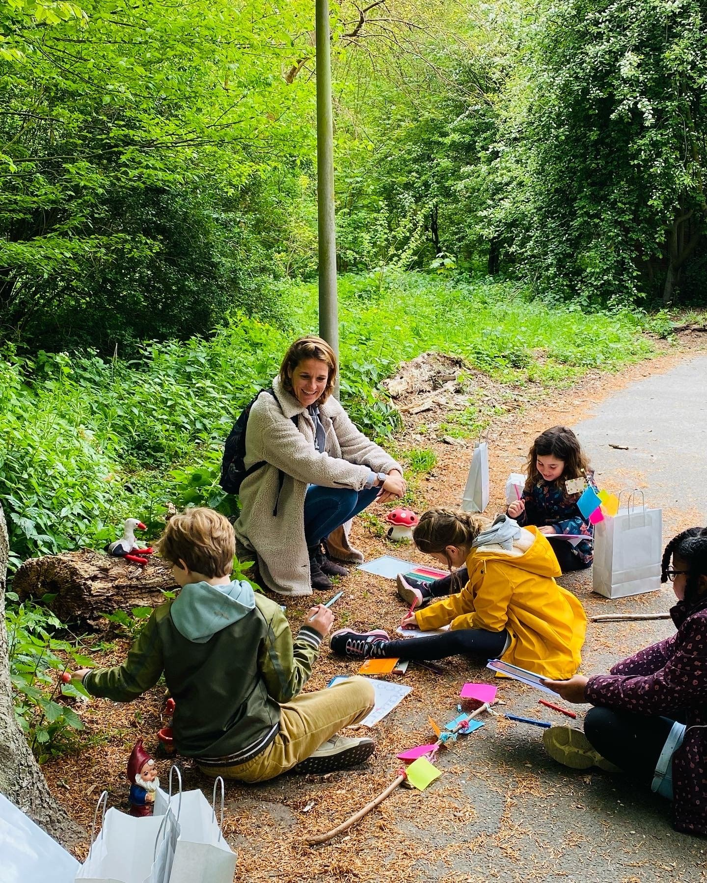 Vrouw met vier kinderen die buiten in een park op papier schetst.