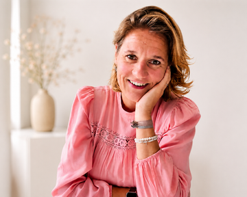 Belinda lacht naar de camera, ze draagt โโeen witte blouse met een blauwe rand.