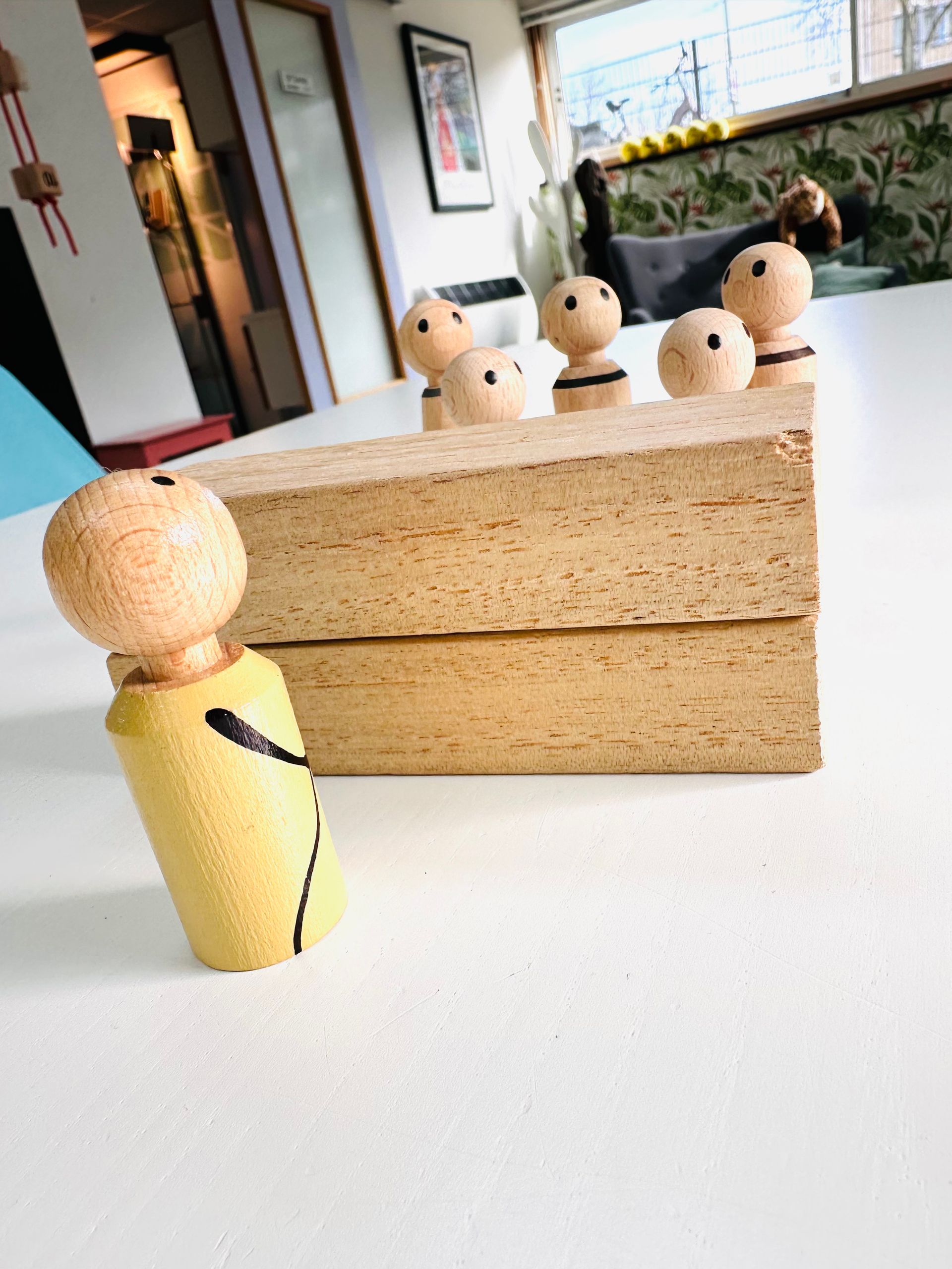 Houten poppetjes, klaar om mee te spelen, staan op een witte ondergrond, één poppetje staat iets naar voren gekanteld, de andere twee staan achter een houten blok.