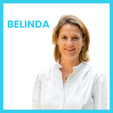 Belinda lacht naar de camera, ze draagt ​​een witte blouse met een blauwe rand.