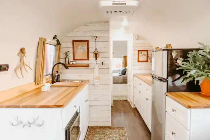 A kitchen in a trailer with white cabinets and wooden counter tops.