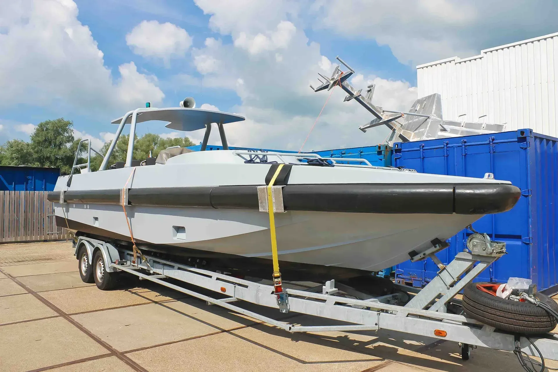 A boat is sitting on a trailer in front of a blue container.