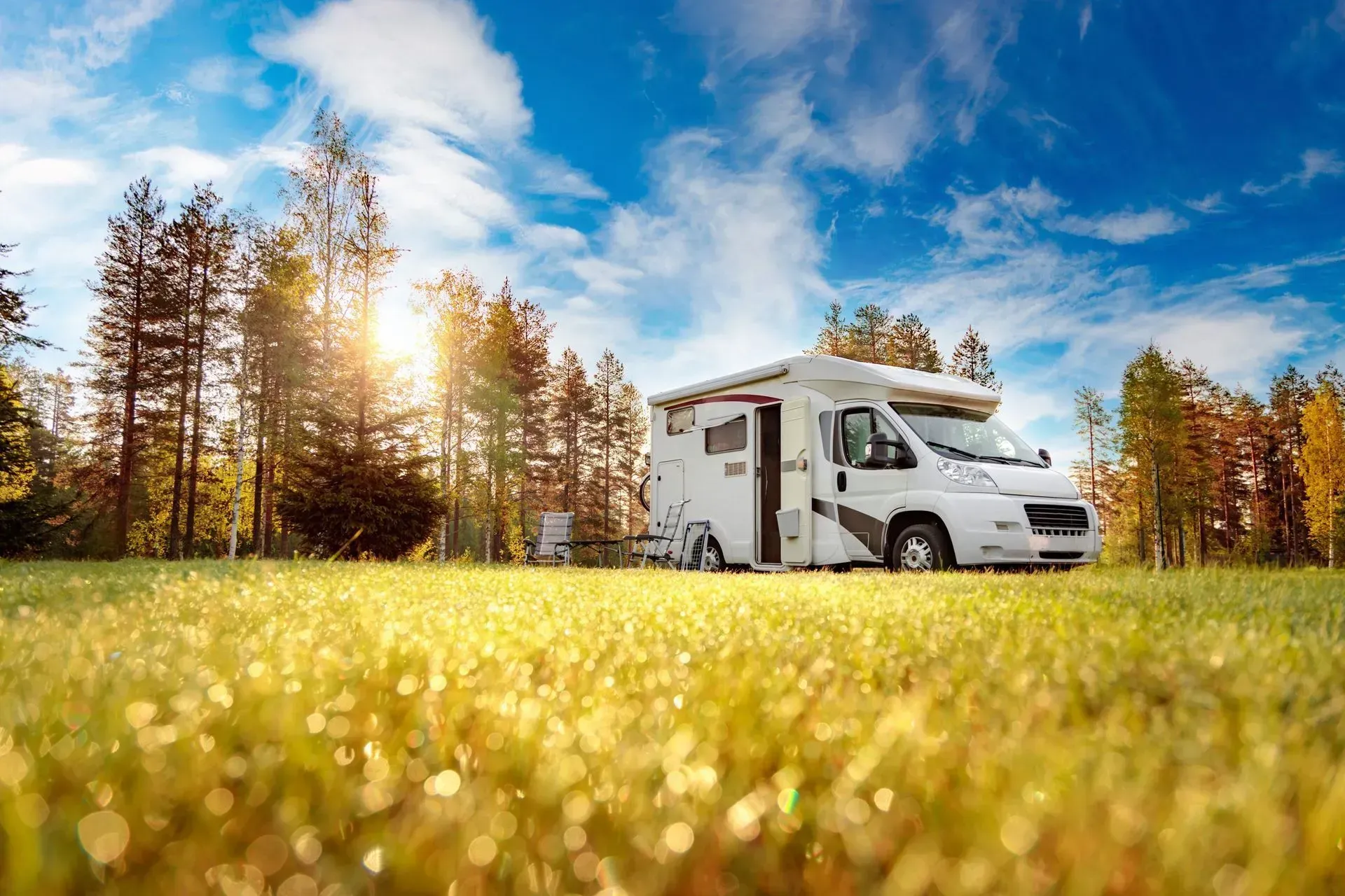 A rv is parked in a grassy field with trees in the background.