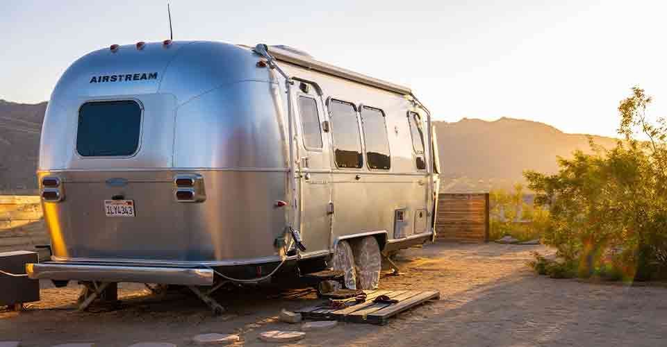 A silver airstream trailer is parked in the middle of a desert.