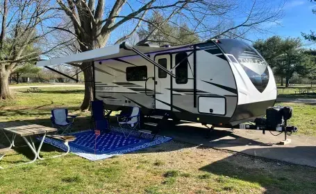 A rv is parked in a grassy area with a picnic table and chairs.