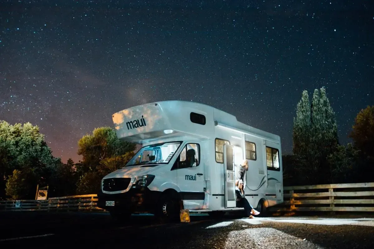 A rv is parked in a parking lot at night under a starry sky.