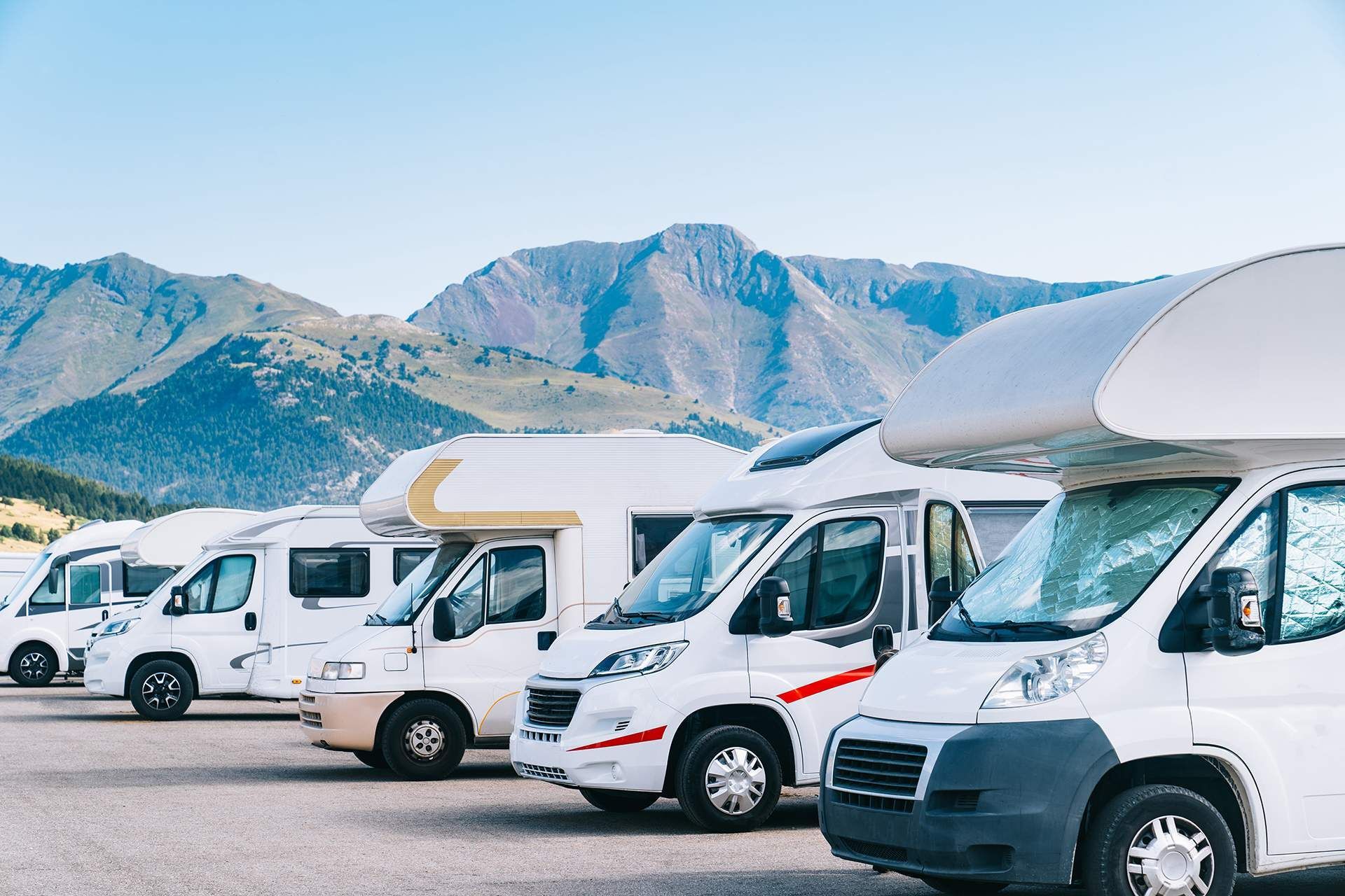 A row of rvs parked in a parking lot with mountains in the background.