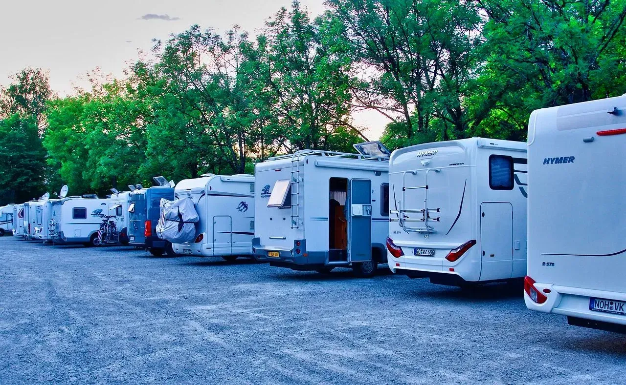 A row of rvs are parked in a gravel lot.