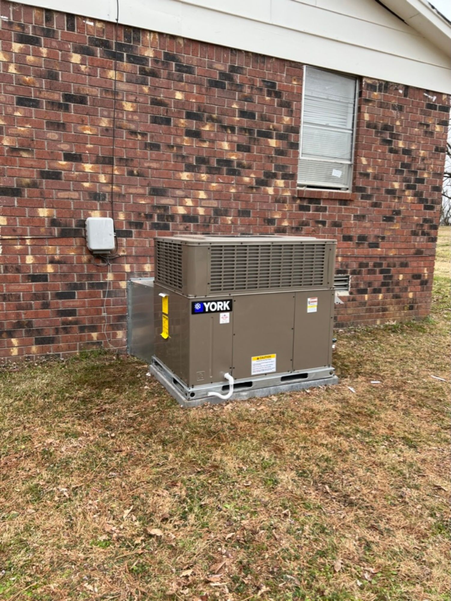 A large air conditioner is sitting on the side of a brick house.