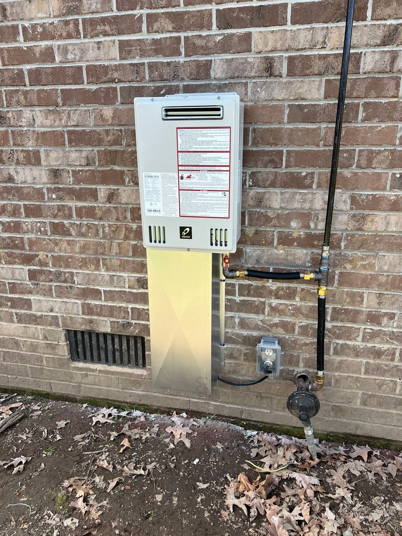 A gas water heater is installed on the side of a brick building.
