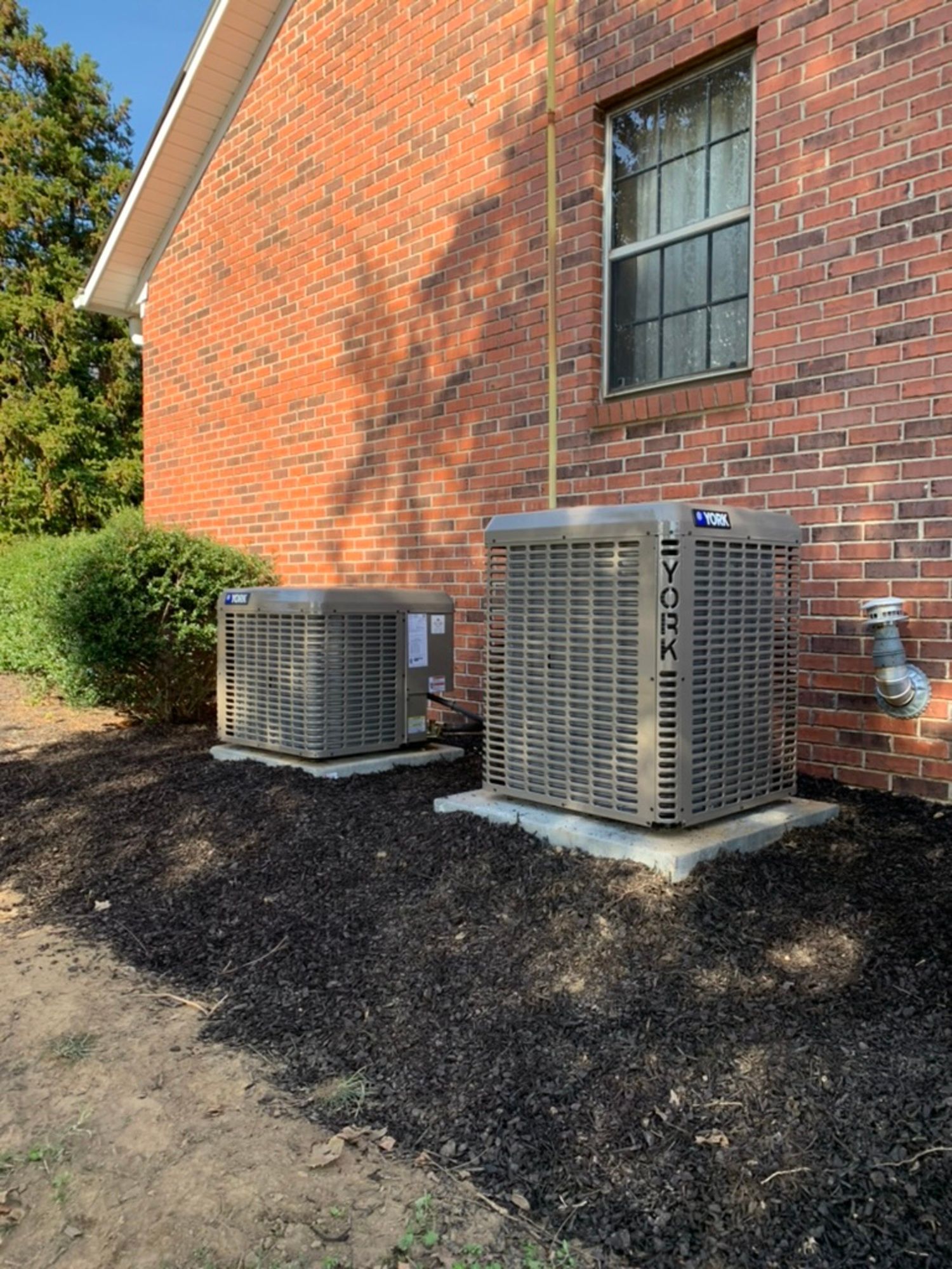 Two air conditioners are sitting on the side of a brick house.