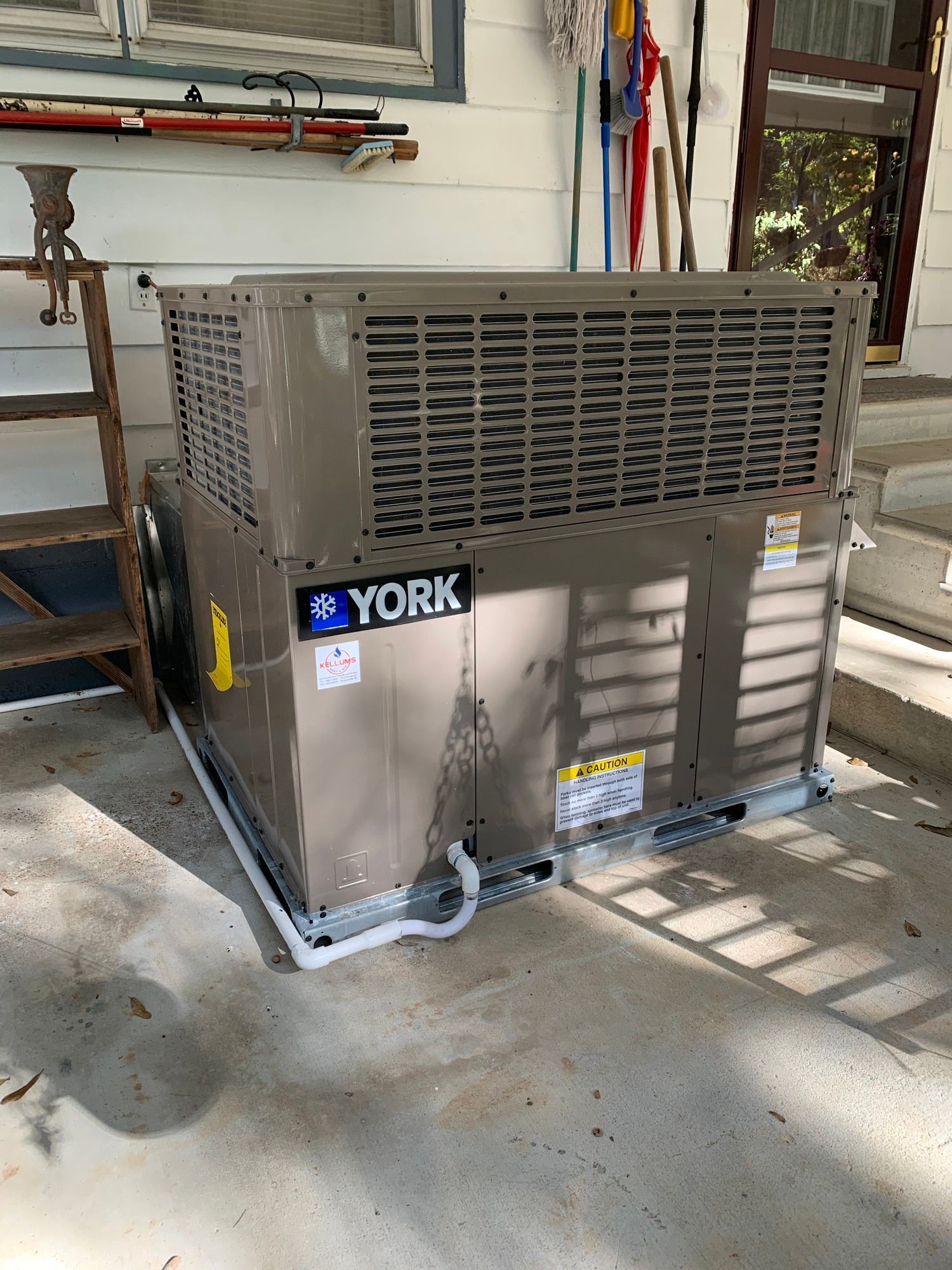 A york air conditioner is sitting on the ground in front of a house.