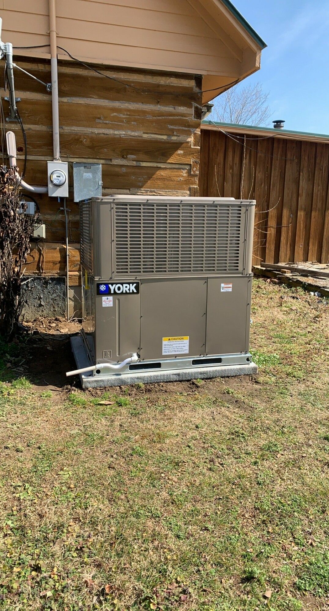 A large air conditioner is sitting in the grass in front of a log cabin.