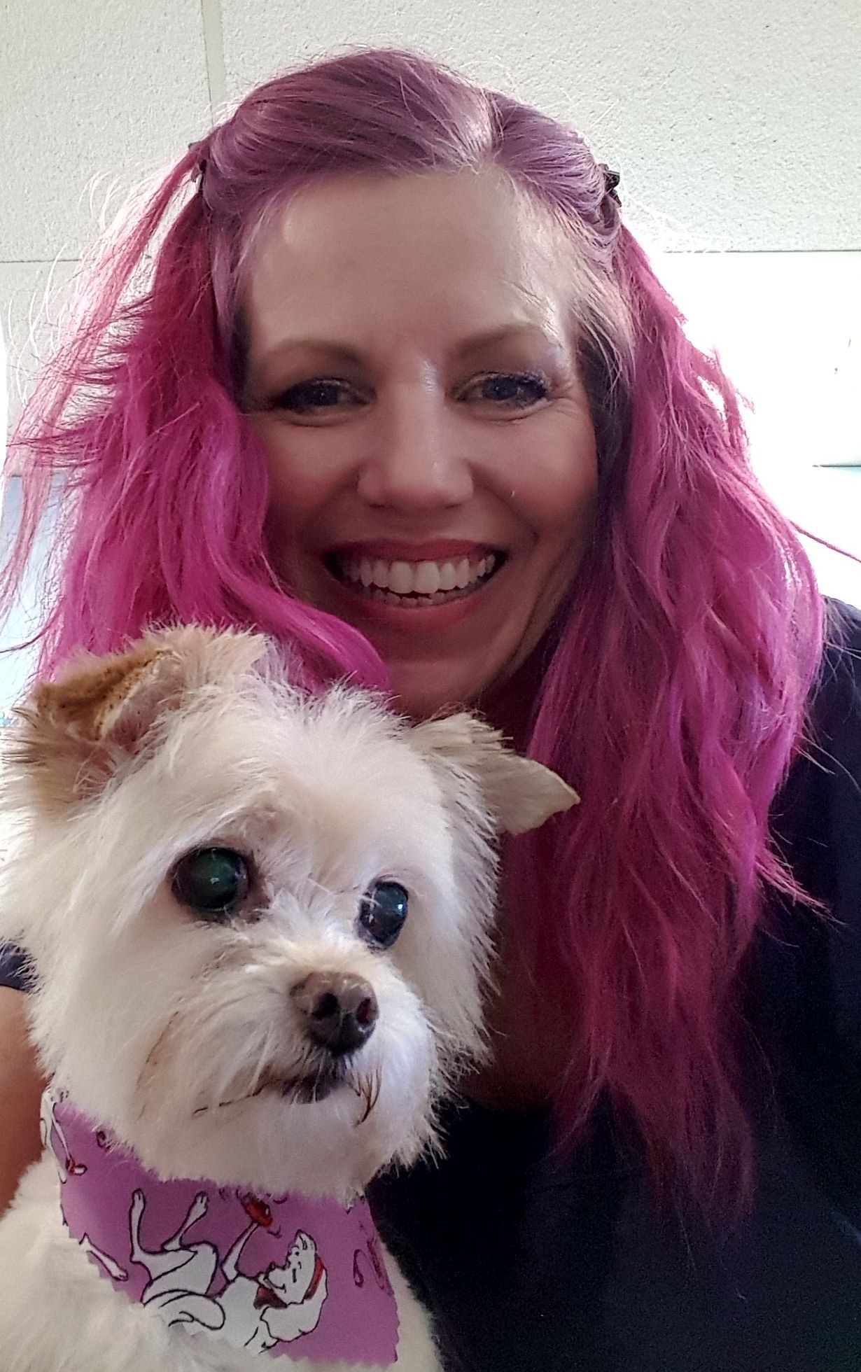 A woman with pink hair is holding a small white dog.