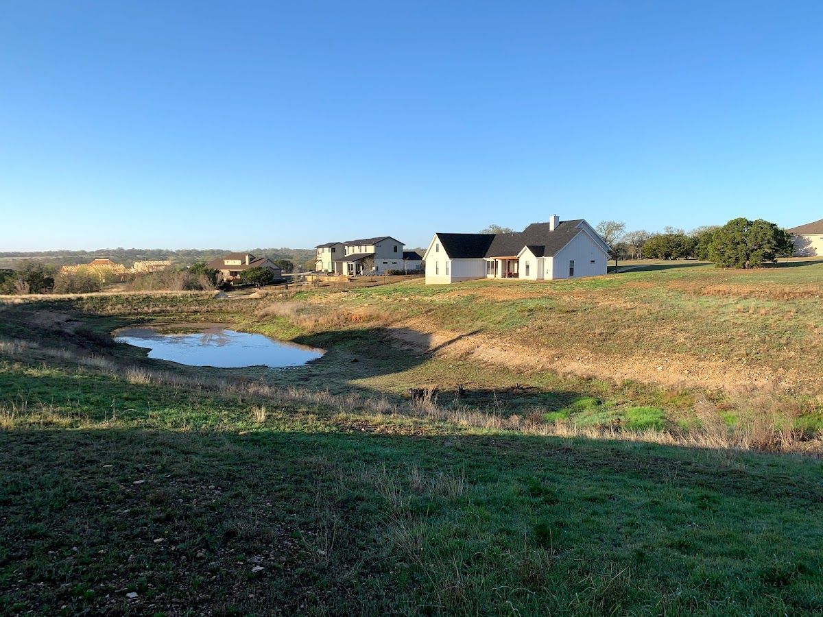 A house is sitting on top of a grassy hill next to a pond.