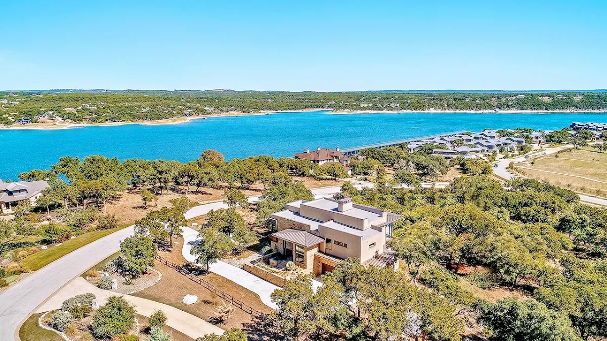 An aerial view of a house next to a lake surrounded by trees.