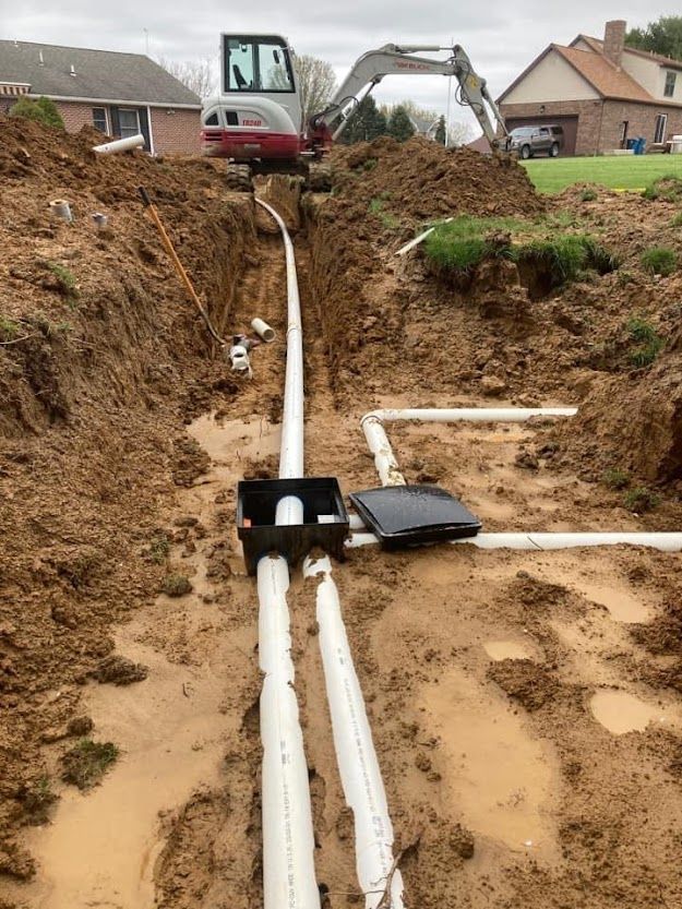 A drain pipe is being installed in a trench next to a house.
