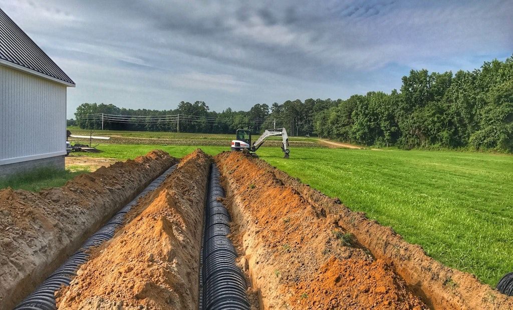Black corrugated pipes laid in rows, possibly for drainage or infrastructure in a dirt field near trees.