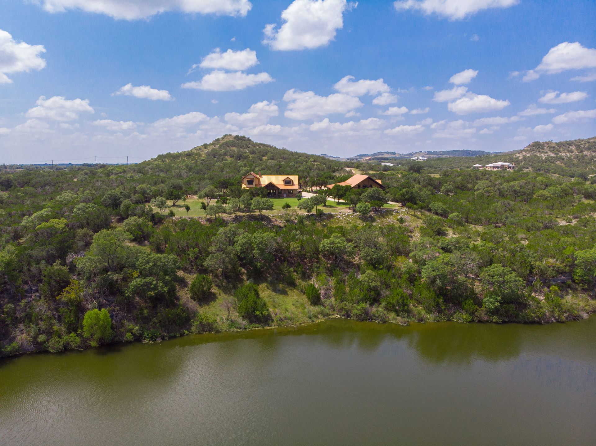 An aerial view of a house on top of a hill next to a lake surrounded by trees.