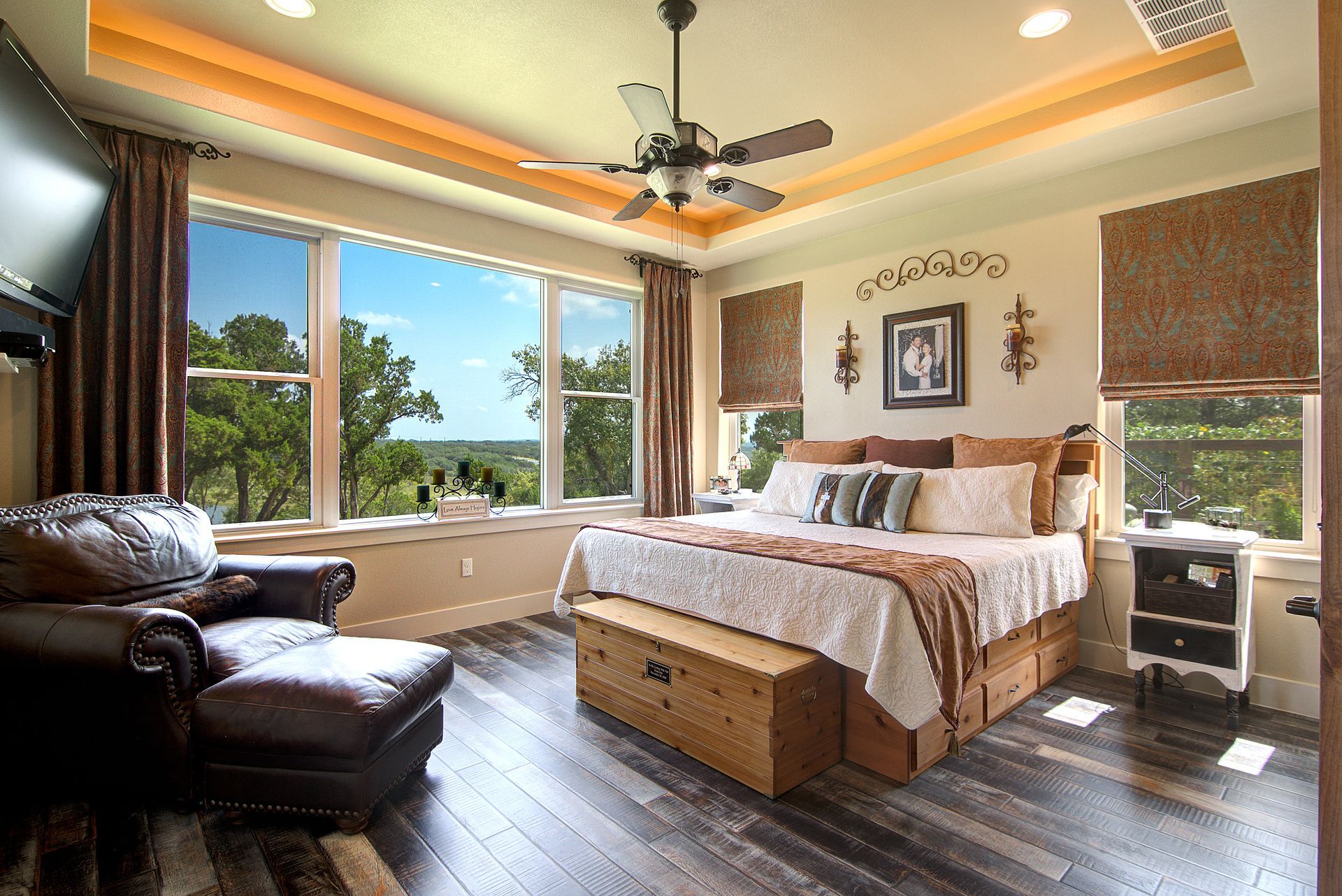 A bedroom with a large bed , chair , ottoman and ceiling fan.