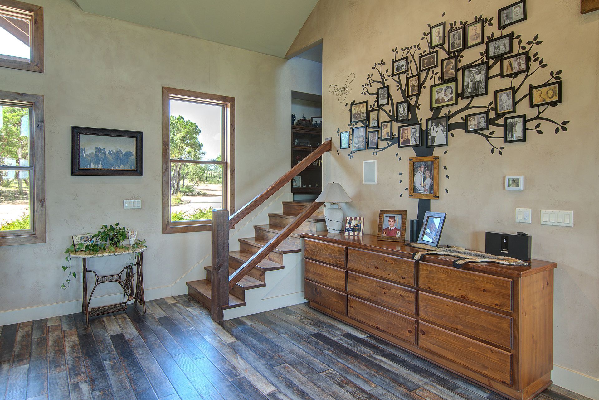 A living room with stairs a dresser and a picture tree on the wall