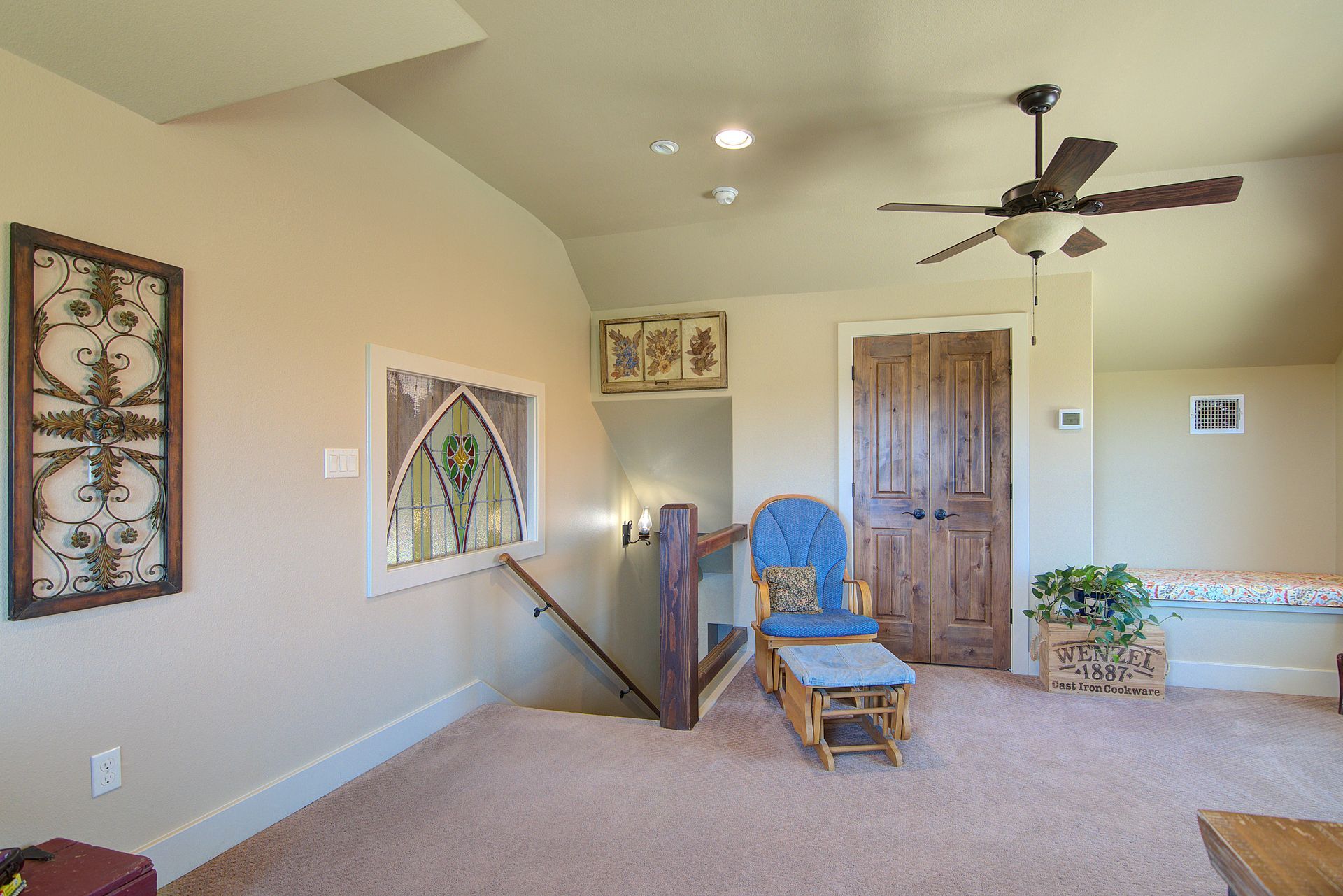 A living room with a ceiling fan , chair , ottoman and stairs.