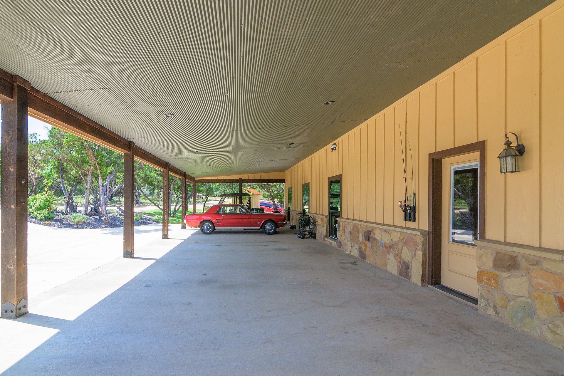A red car is parked under a covered porch of a building.