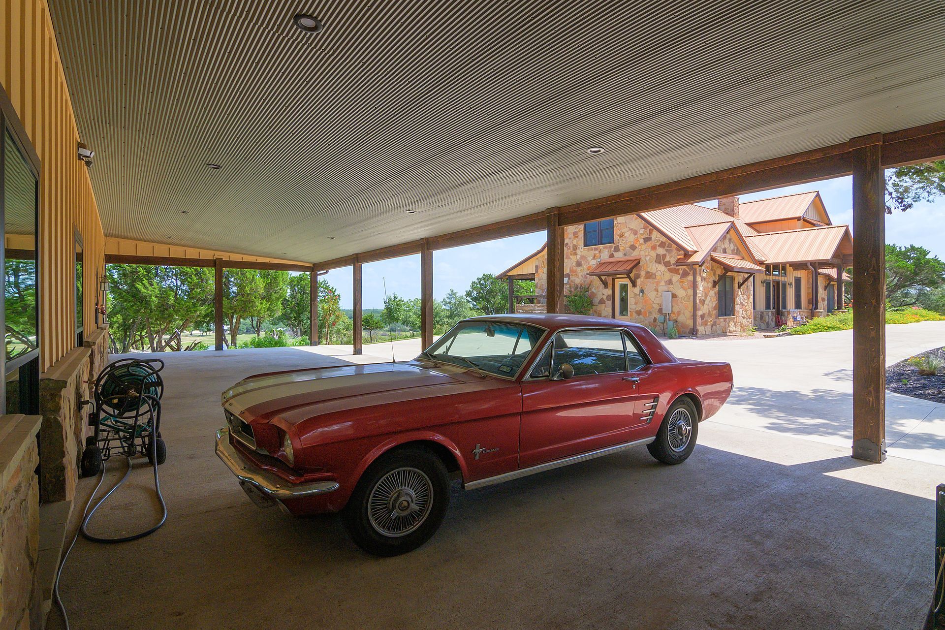 A red mustang is parked in a carport under a canopy.