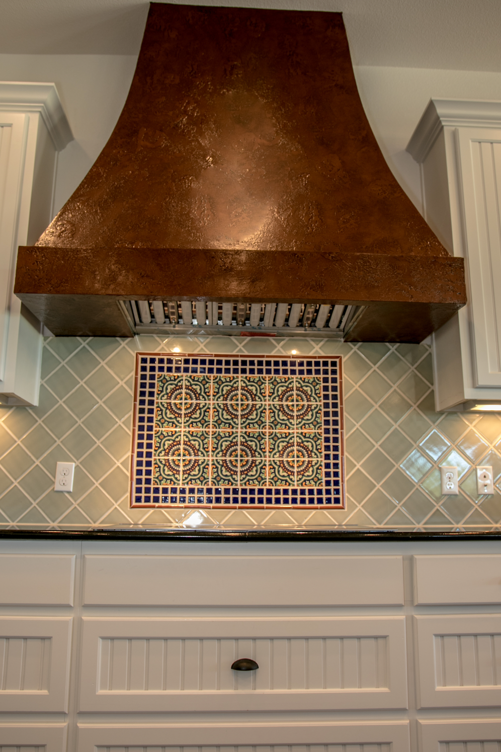 A kitchen with a copper hood and a mosaic on the wall.