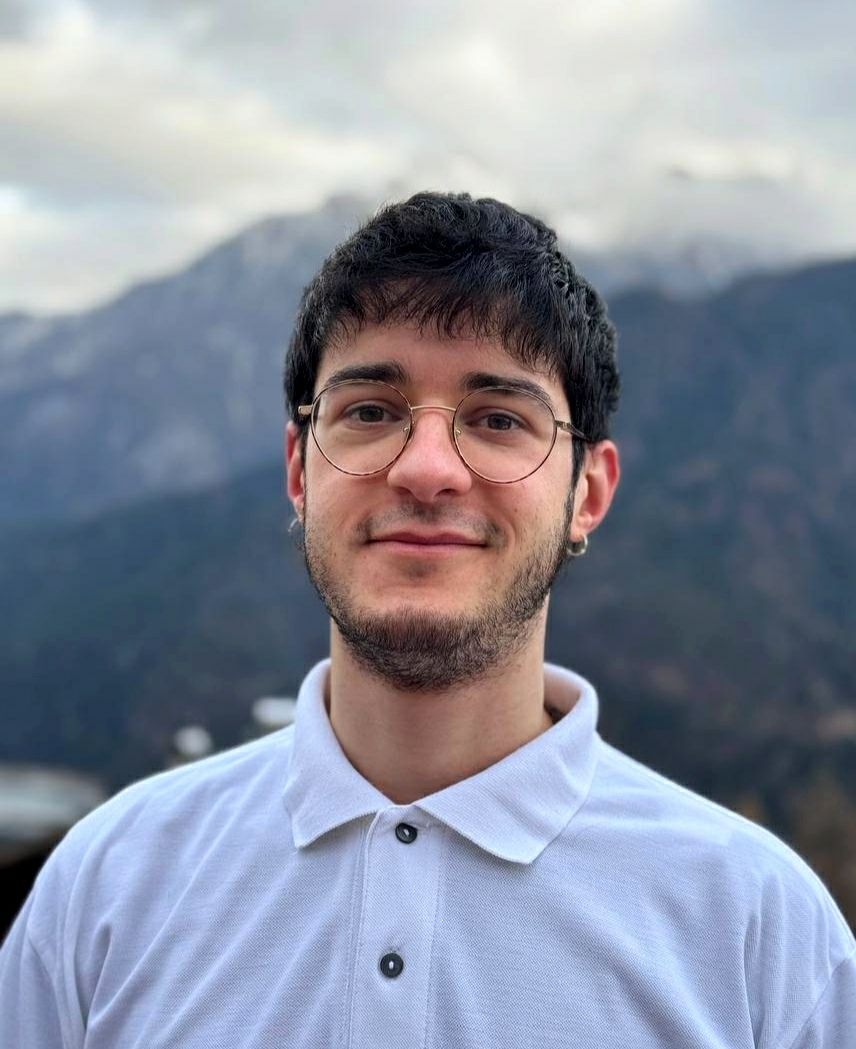 Un giovane che indossa occhiali e una polo bianca è in piedi di fronte a una montagna.