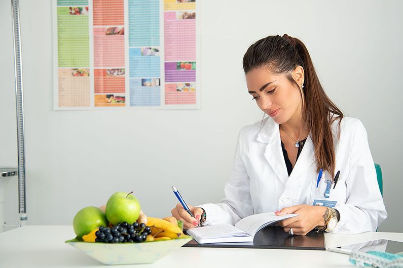 Una donna in camice è seduta a una scrivania con una ciotola di frutta.
