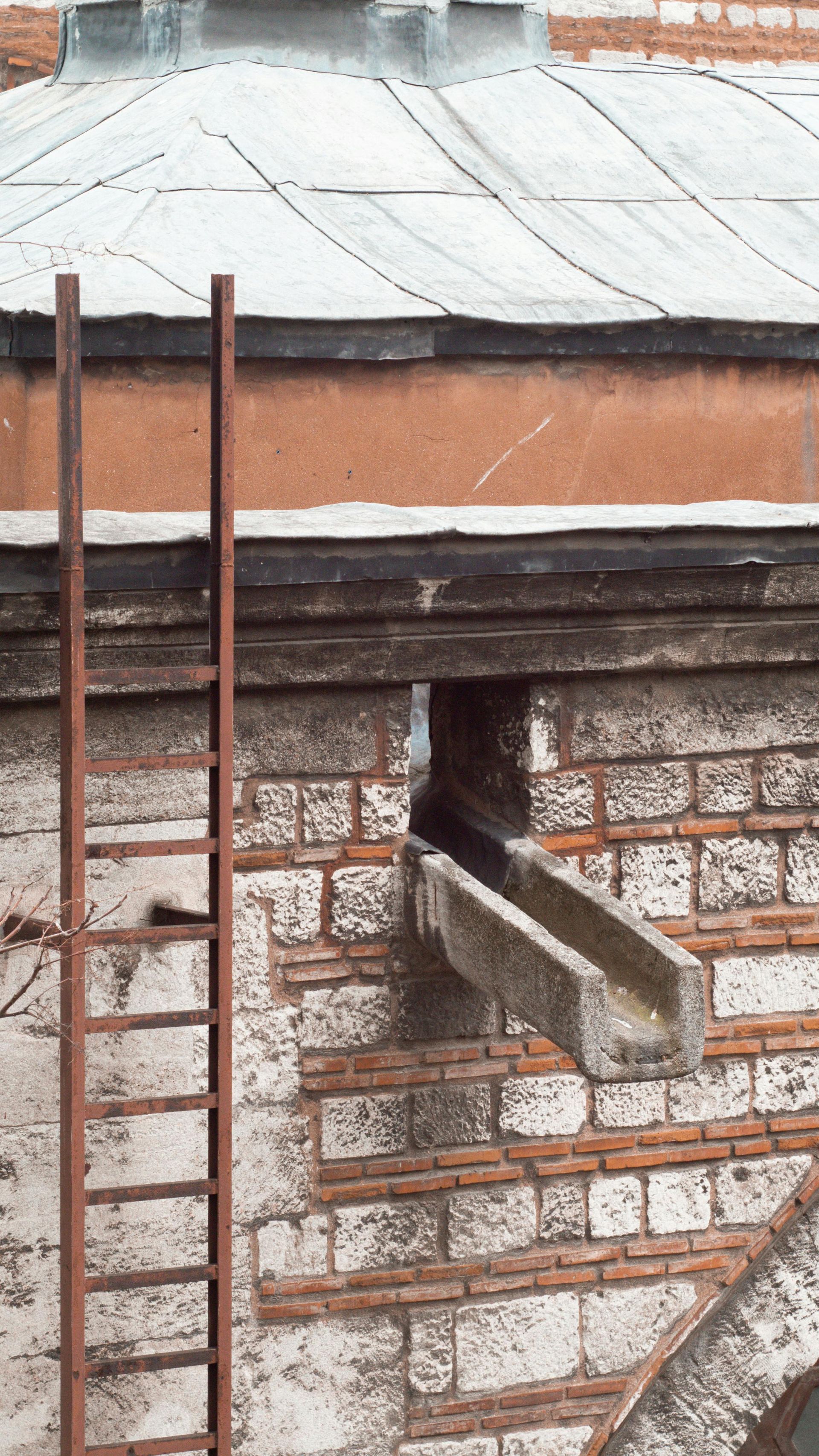 Red brick and stone building with a metal gutter and rusty ladder attached to the side.