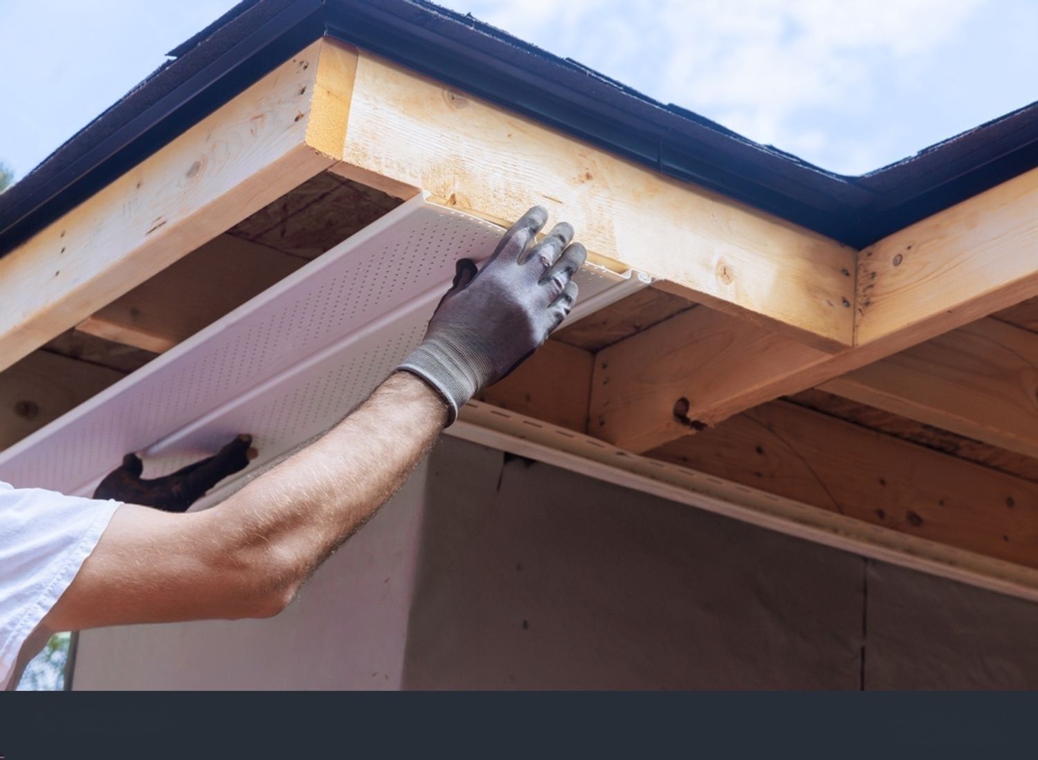 Person installing white perforated soffit panel to wooden structure.