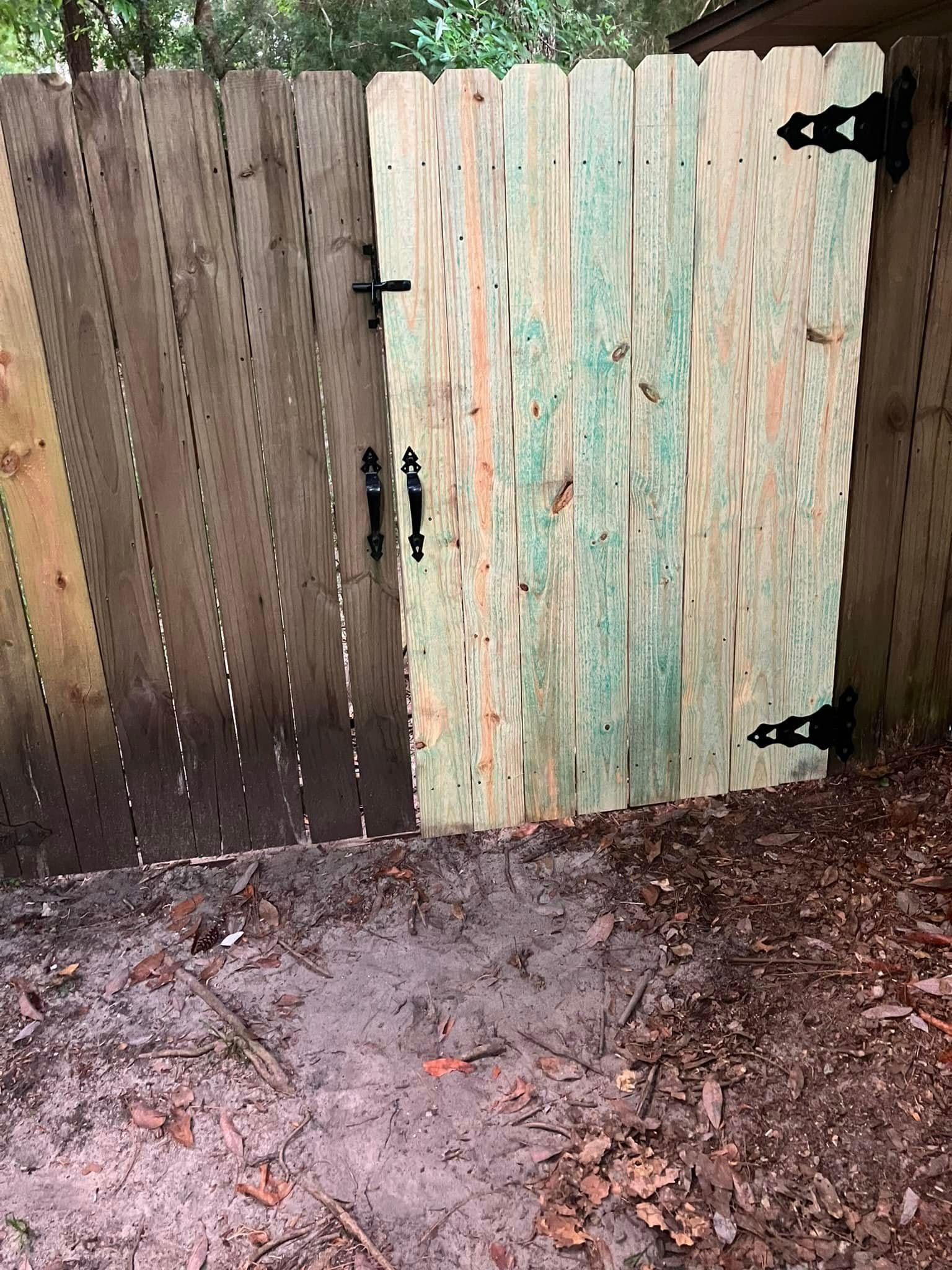 Wooden fence gate with black hardware; gate is weathered green.