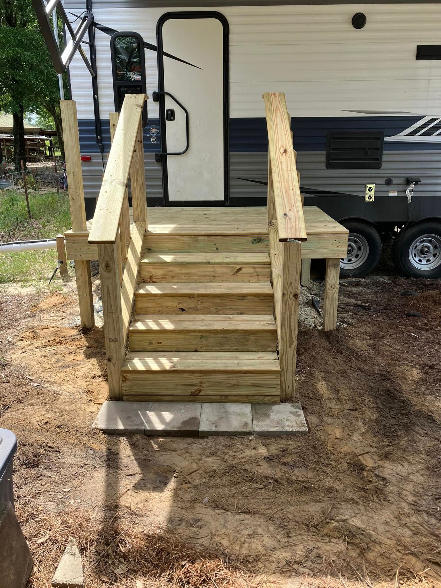 Wooden stairs leading to a camper door, with a handrail on both sides.