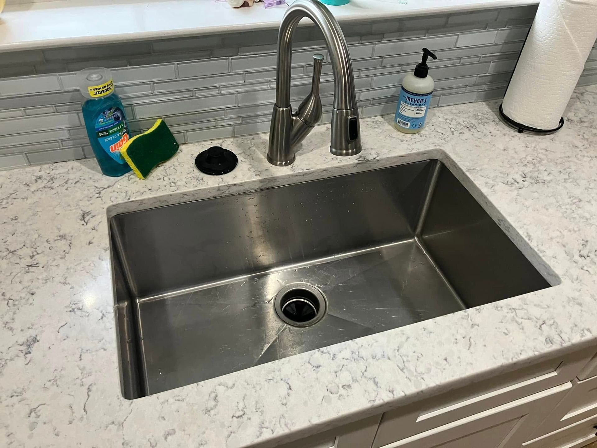 Stainless steel kitchen sink with faucet on a marble countertop. Soap and sponge are visible.