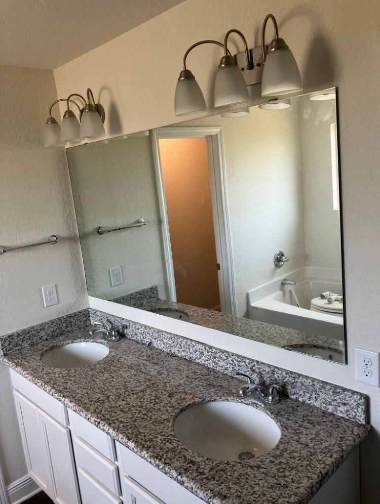 Bathroom with double vanity, granite countertop, large mirror, and white cabinets.