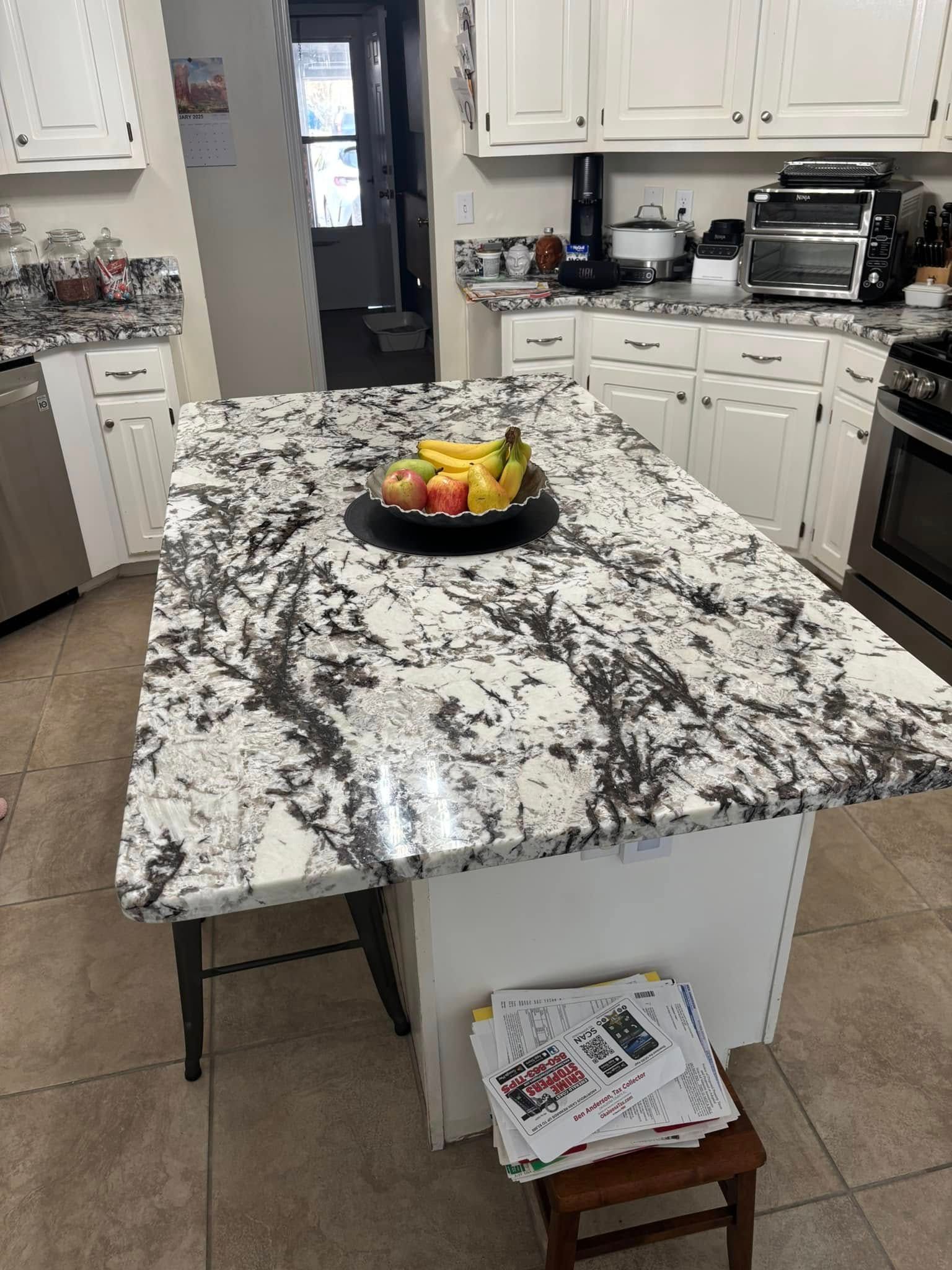 Kitchen island with granite countertop, fruit bowl, and white cabinets.