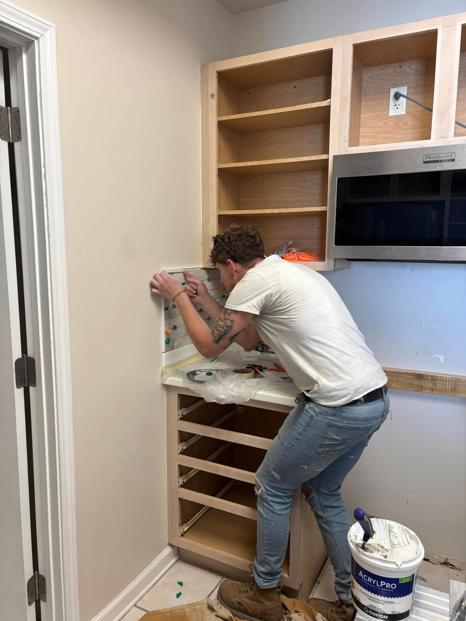 Man installing something in a kitchen cabinet with shelves, next to a built-in oven.