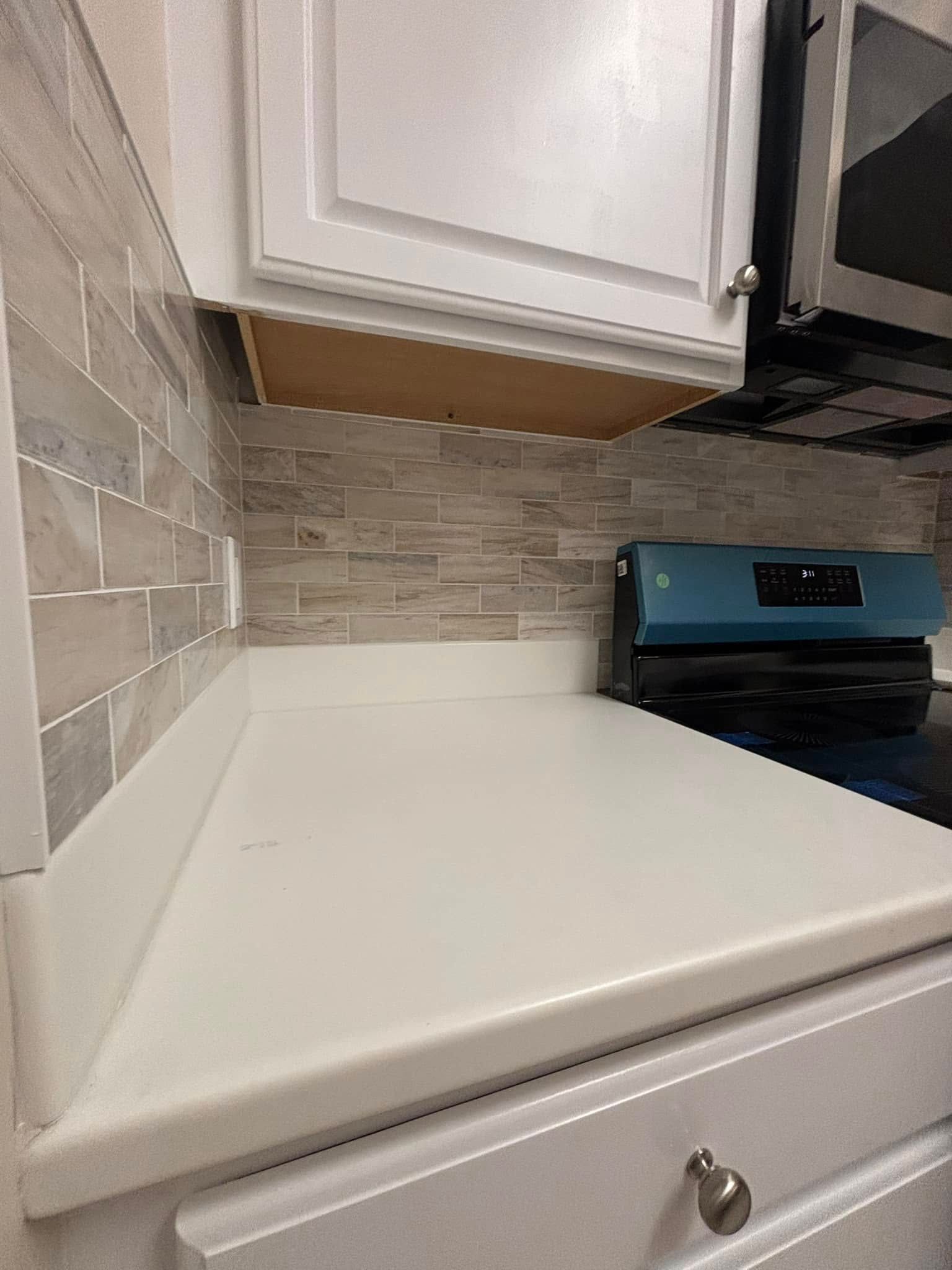 White kitchen countertop, backsplash, stove, and cabinets.