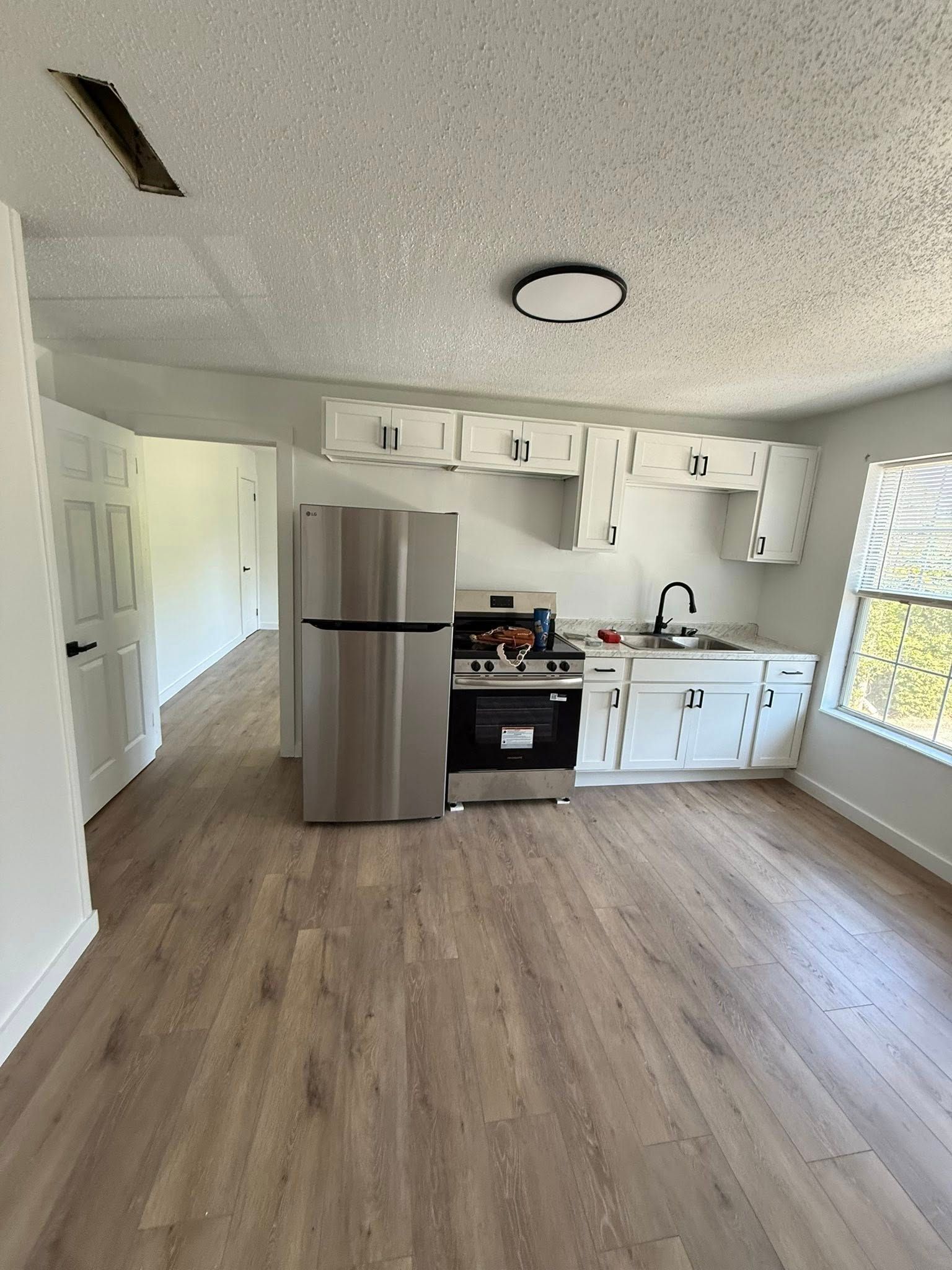 A small, newly renovated kitchen with stainless steel appliances, white cabinets, and laminate flooring.