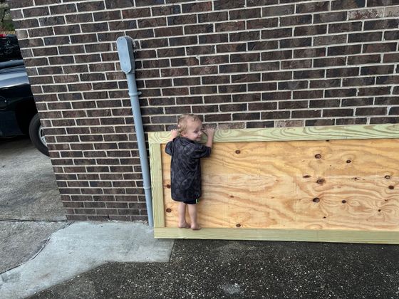 Yellow building with pergola, deck, and railing overlooking a pond with green plants and a clear blue sky.