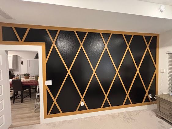 Black wall with gold diamond pattern, open doorway to a kitchen.