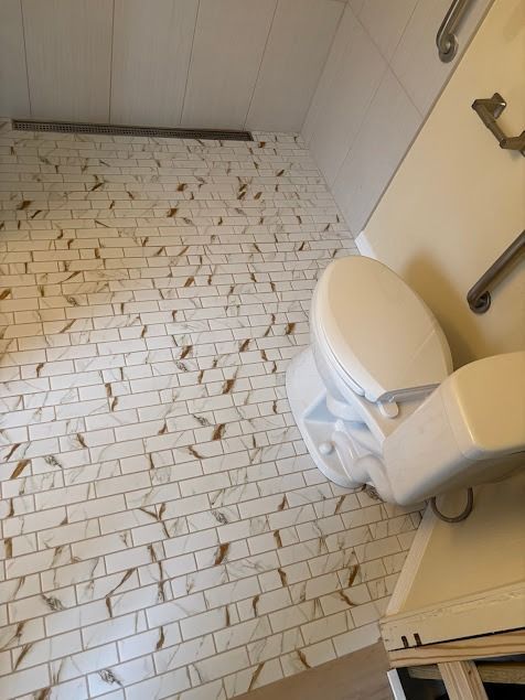 Bathroom with white and gold tile floor, white toilet, and grab bars.