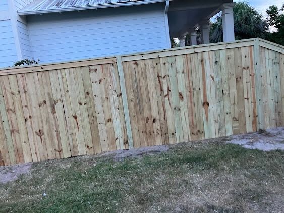 Wooden fence bordering a lawn next to a light blue house.